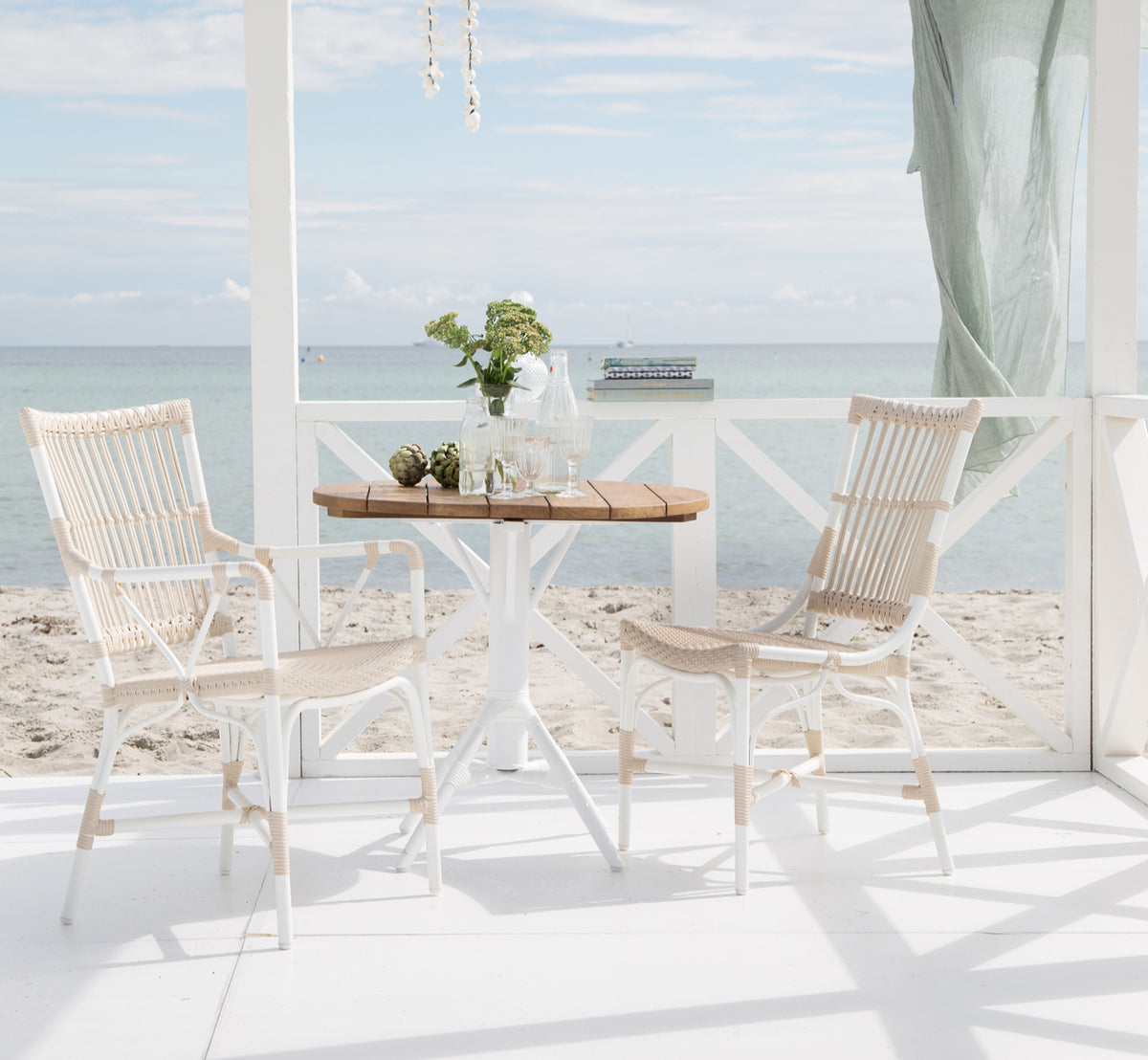Dies ist ein Lifestyle-Bild von Piano Exterior Side Chair i dove white aluminium artfibre. In einem Essbereich unter einer Pergola am Meer.