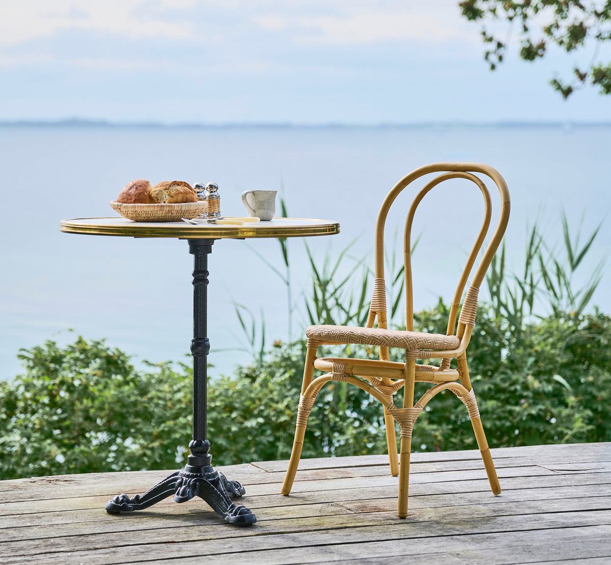 Dies ist ein Lifestyle-Bild von Lulu Außen-Esszimmerstuhl in natural aluminium artfibre. An einem Bistrotisch am Wasser mit Gebäck und ruhigem Meer.