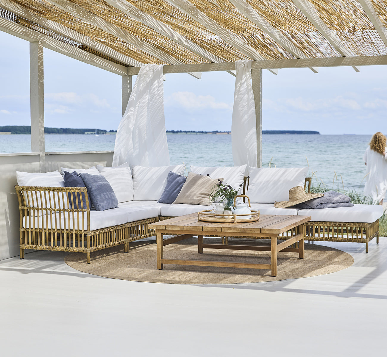 Dies ist ein Lifestyle-Bild von Maggie Sofa Mittelmodul in antique aluminium artfibre. Strandpavillon mit Modulsofa und Meerblick.