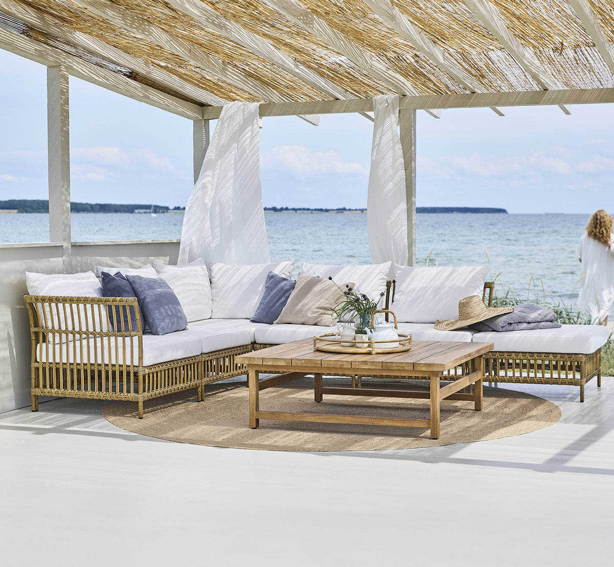 Dies ist ein Lifestyle-Bild von Maggie Sofa Mittelmodul in antique aluminium artfibre. Strandpavillon mit Modulsofa und Meerblick.