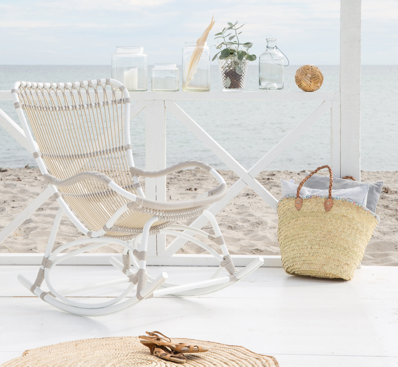 Dies ist ein Lifestyle-Bild von Monet Exterior Rocking Chair i dove white aluminium artfibre. In einem Strandpavillon mit Meerblick.