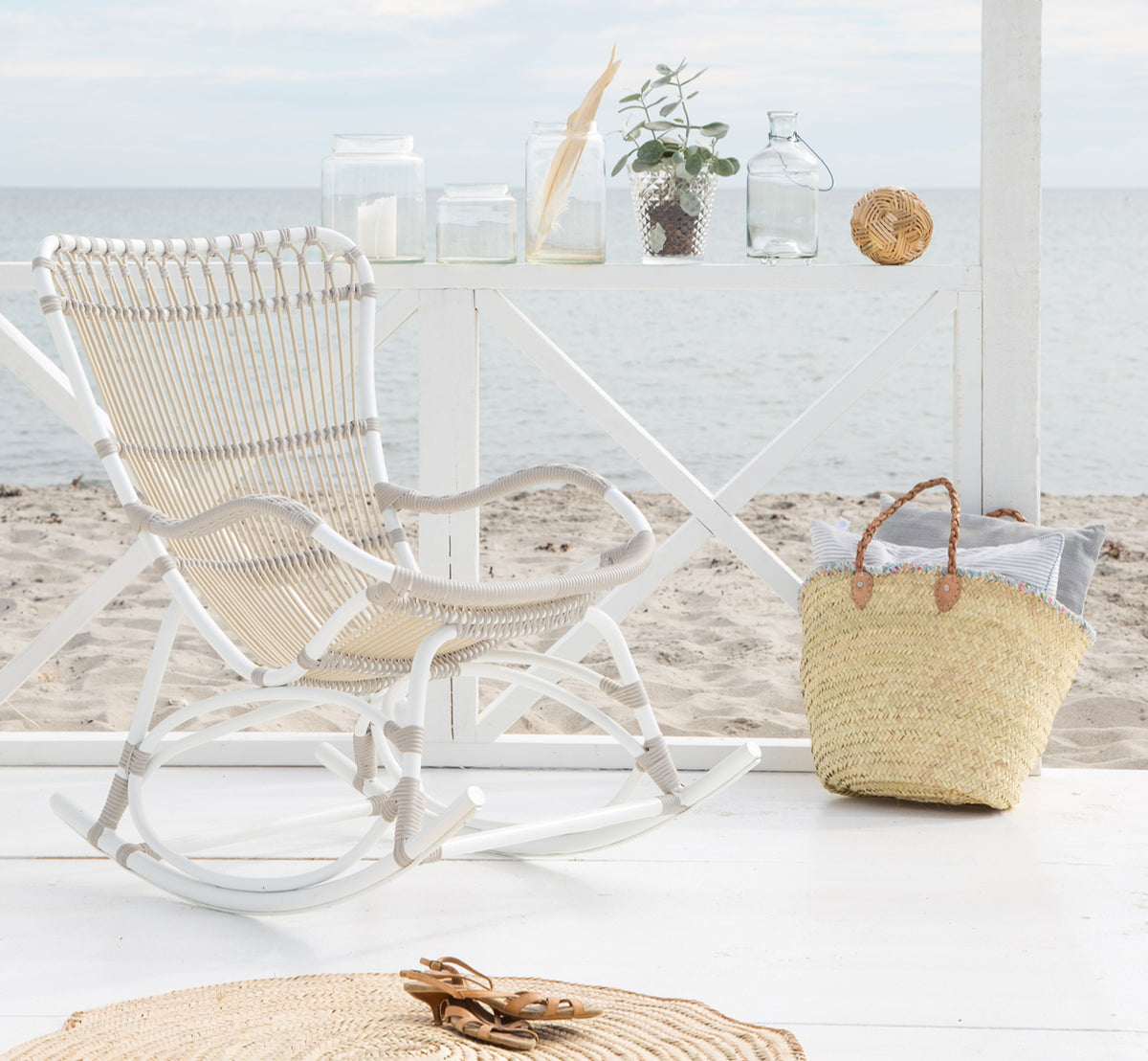 Dies ist ein Lifestyle-Bild von Monet Exterior Rocking Chair i dove white aluminium artfibre. In einem Strandpavillon mit Meerblick.