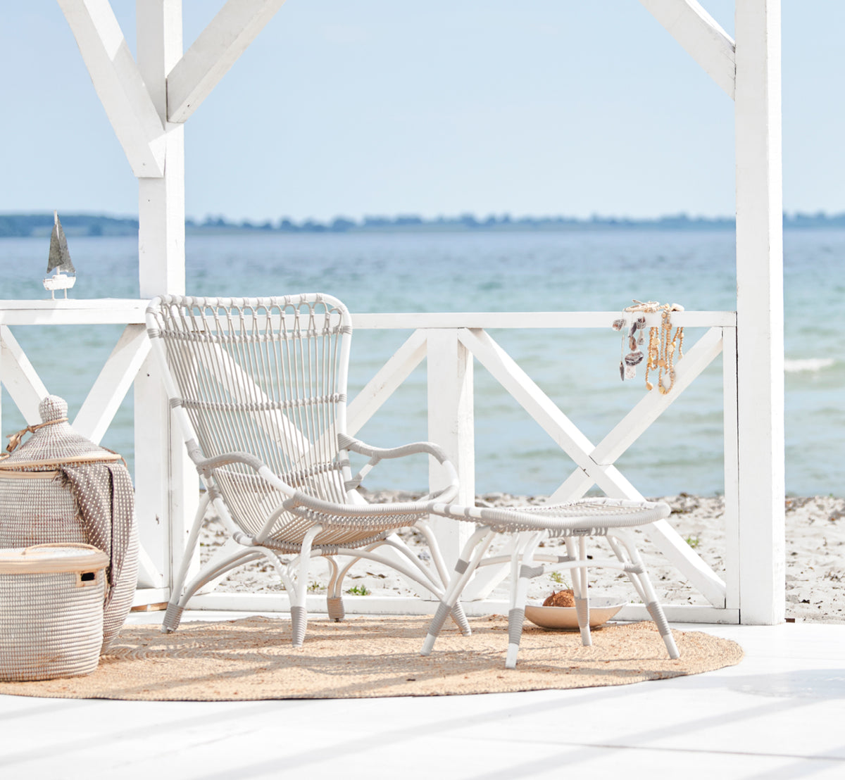 Dies ist ein Lifestyle-Bild von Monet Exterior Lounge Chair i dove white aluminium artfibre. In einem Strandpavillon mit Juteteppich.