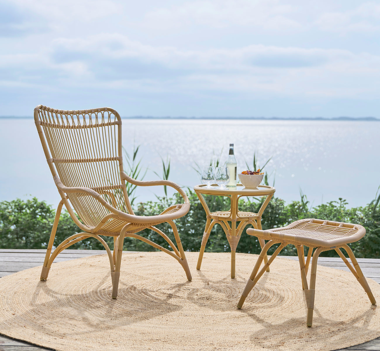Dies ist ein Lifestyle-Bild von Monet Exterior Lounge Chair i natural aluminium artfibre. Mit Fußhocker auf einem Deck mit Blick auf das Meer.