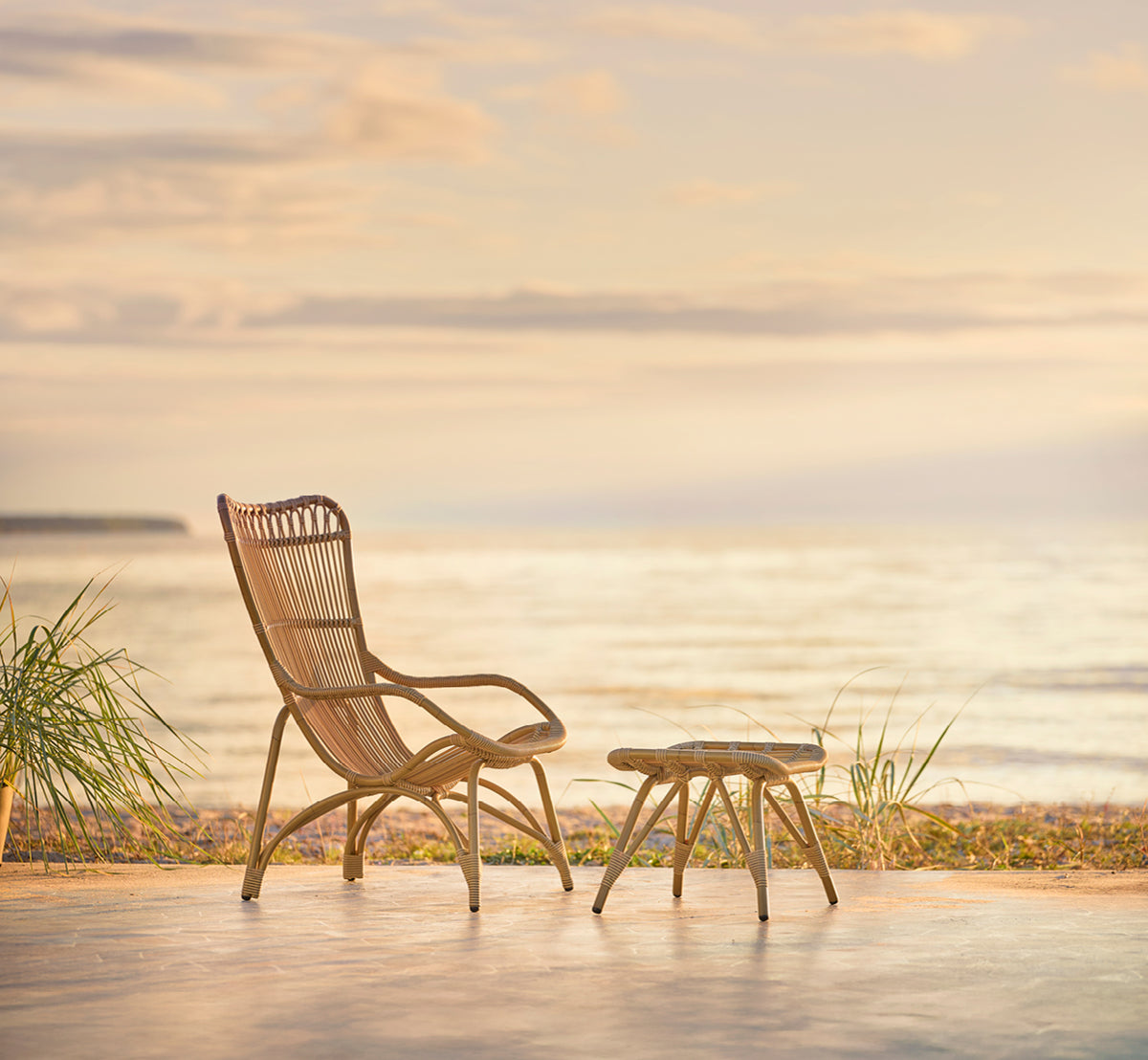 Dies ist ein Lifestyle-Bild von Monet Exterior Footstool i antique aluminium artfibre. Mit Lounge-Sessel auf einem Strandpavillon-Deck.