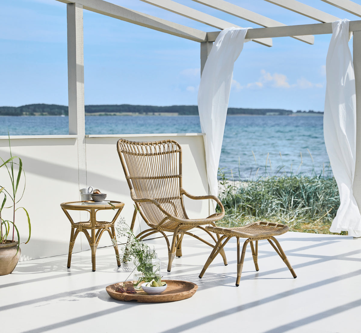 Dies ist ein Lifestyle-Bild von Tony Exterior Side Table i antique aluminium artfibre. Neben einem Lounge-Sessel in einem Strandpavillon.
