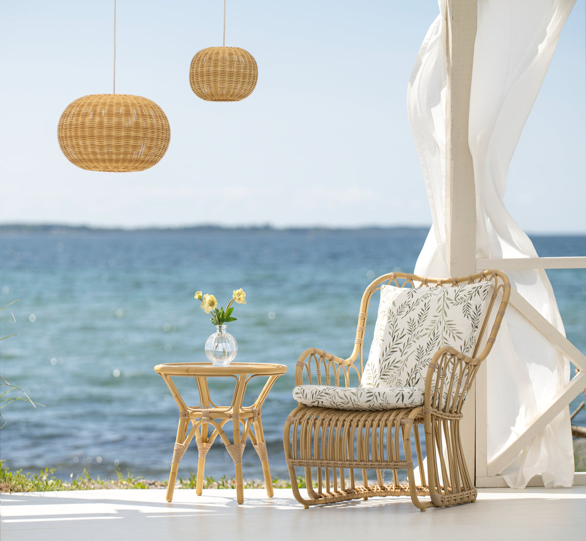 Dies ist ein Lifestyle-Bild von Tony Exterior Side Table i natural aluminium artfibre. Neben einem Lounge-Sessel auf einem Deck am Meer.