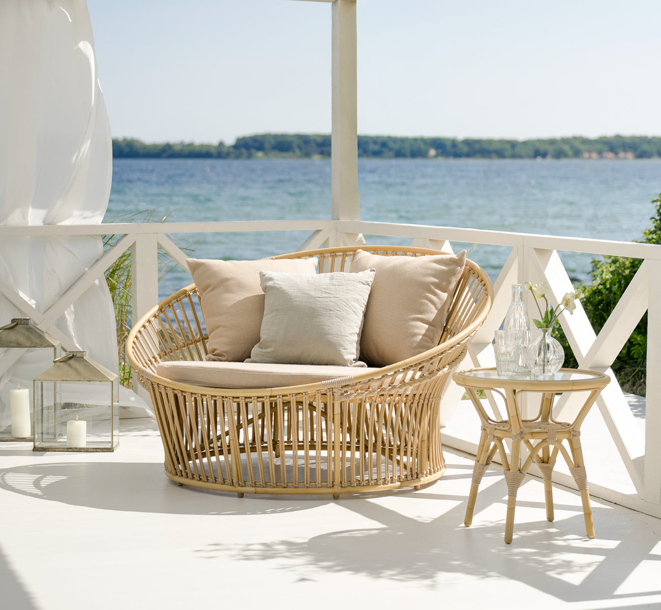 Dies ist ein Lifestyle-Bild von Tony Exterior Side Table i natural aluminium artfibre. Auf einem Holzdeck mit Juteteppich am Meer.