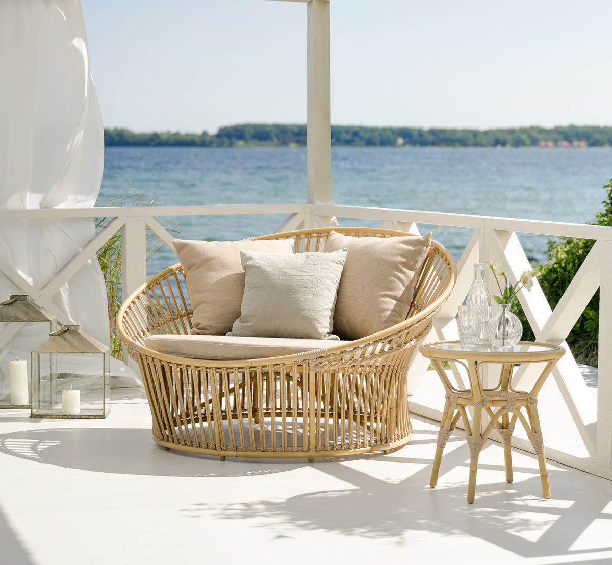 Dies ist ein Lifestyle-Bild von Tony Exterior Side Table i natural aluminium artfibre. Auf einem Holzdeck mit Juteteppich am Meer.
