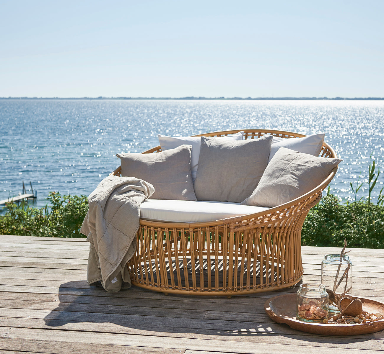 Dies ist ein Lifestyle-Bild von Olympia Nest Exterior i natural aluminium artfibre. In einem Strandpavillon mit Kissen und Meerblick.