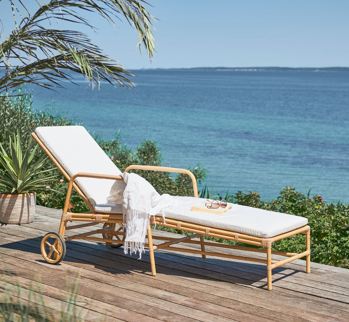 Dies ist ein Lifestyle-Bild von Josephine Sonnenliege in natural aluminium artfibre, auf einer Steintedrasse an der Küste bei Sonnenuntergang mit.