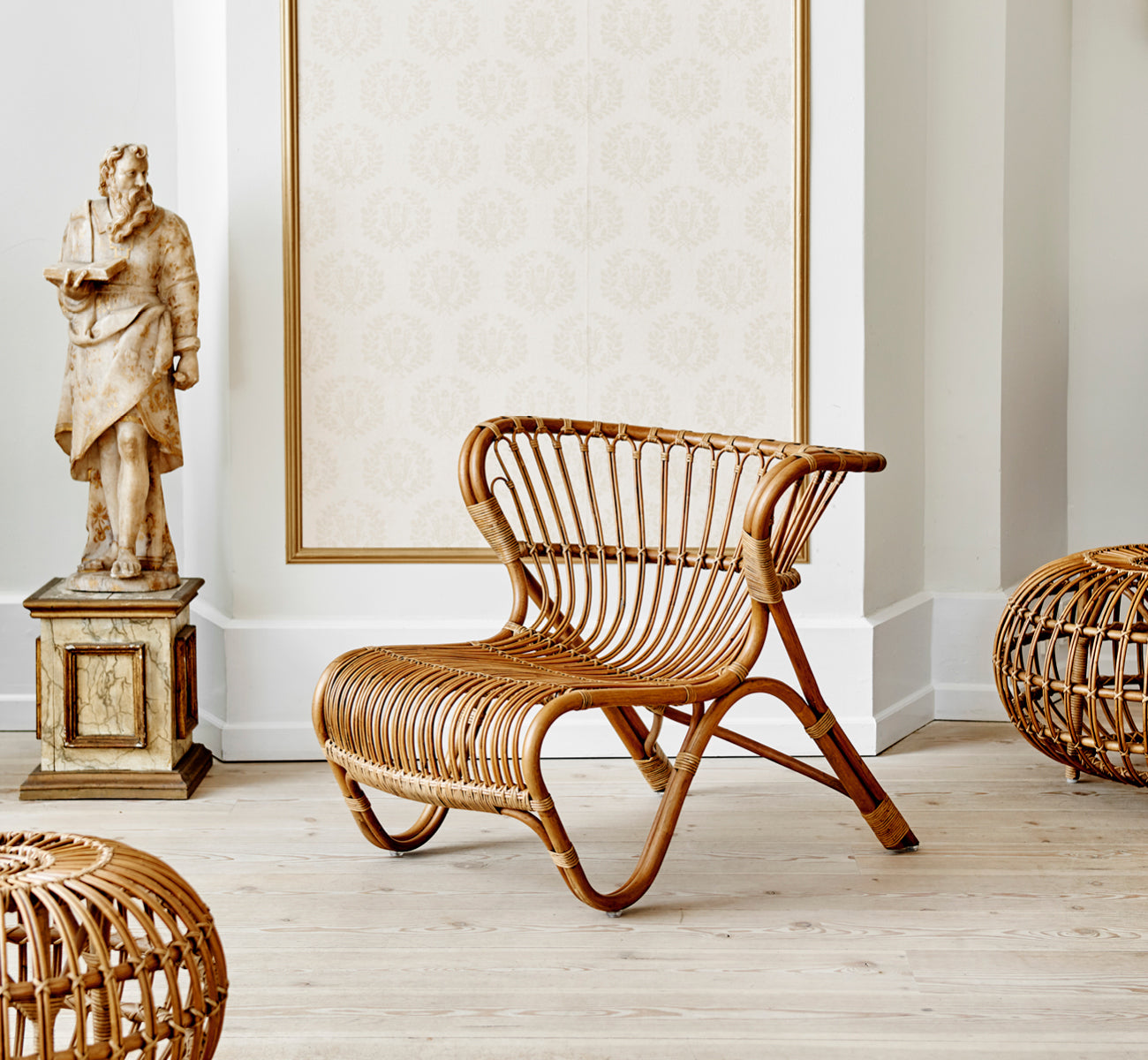 Dies ist ein Lifestyle-Bild von Fox Lounge-Sessel in polished Antique Rattan, in einem warmen Interieur mit ockerfarbener Wandvertäfelung und dunklem.