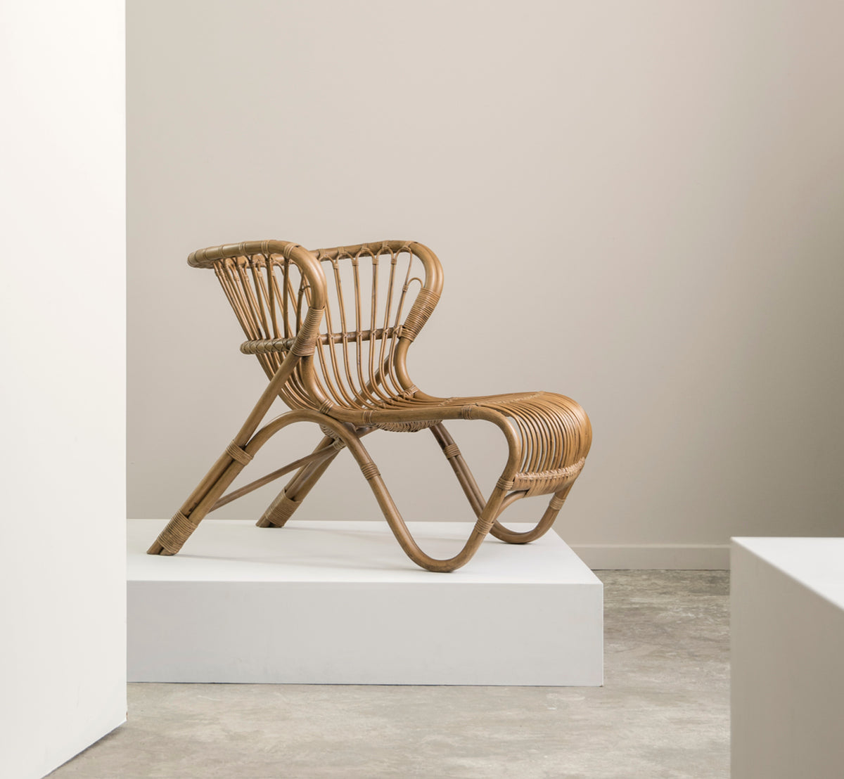 Dies ist ein Lifestyle-Bild von Fox Lounge-Sessel in polished Antique Rattan, in einem warmen Interieur mit ockerfarbener Wandvertäfelung und dunklem.