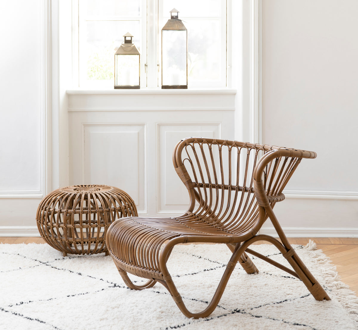 Dies ist ein Lifestyle-Bild von Fox Lounge-Sessel in polished Antique Rattan, in einem warmen Interieur mit ockerfarbener Wandvertäfelung und dunklem.