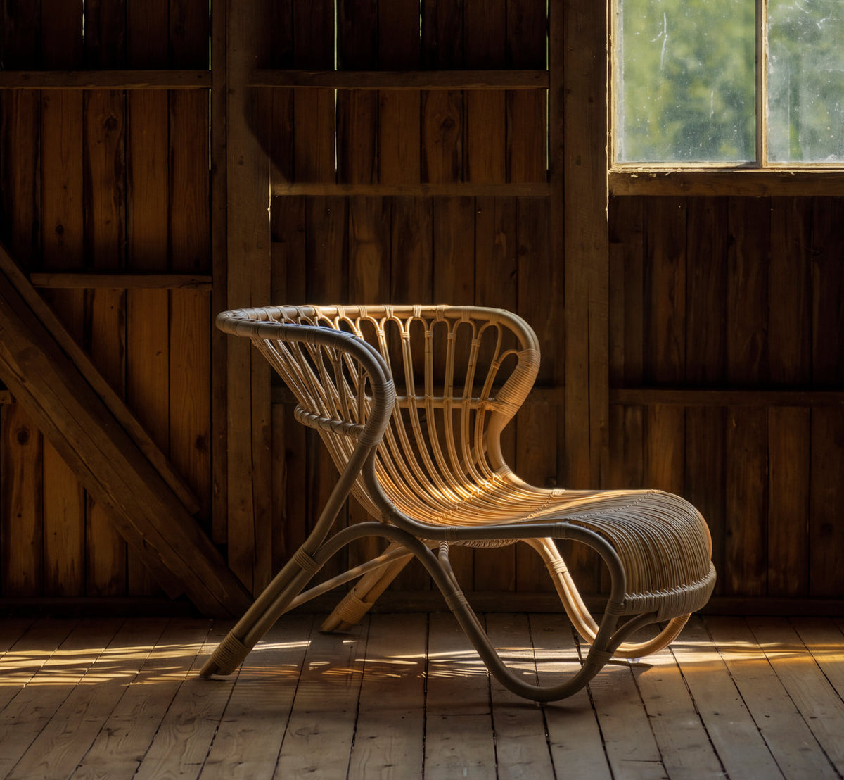 Dies ist ein Lifestyle-Bild von Fox Lounge-Sessel in polished natural rattan. In einer Holzscheune mit warmem Fensterlicht.