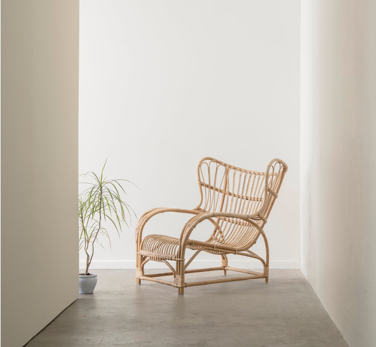 Dies ist ein Lifestyle-Bild von Teddy Lounge-Sessel in polished natural rattan. Auf einem Fischgrätboden an einem Vorhangfenster mit kleinem Spiegel platziert.