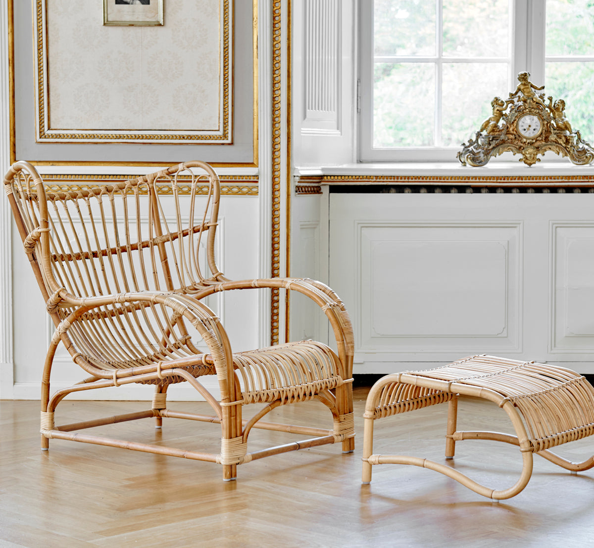 Dies ist ein Lifestyle-Bild von Teddy Lounge-Sessel in polished natural rattan. Auf einem Fischgrätboden an einem Vorhangfenster mit kleinem Spiegel platziert.
