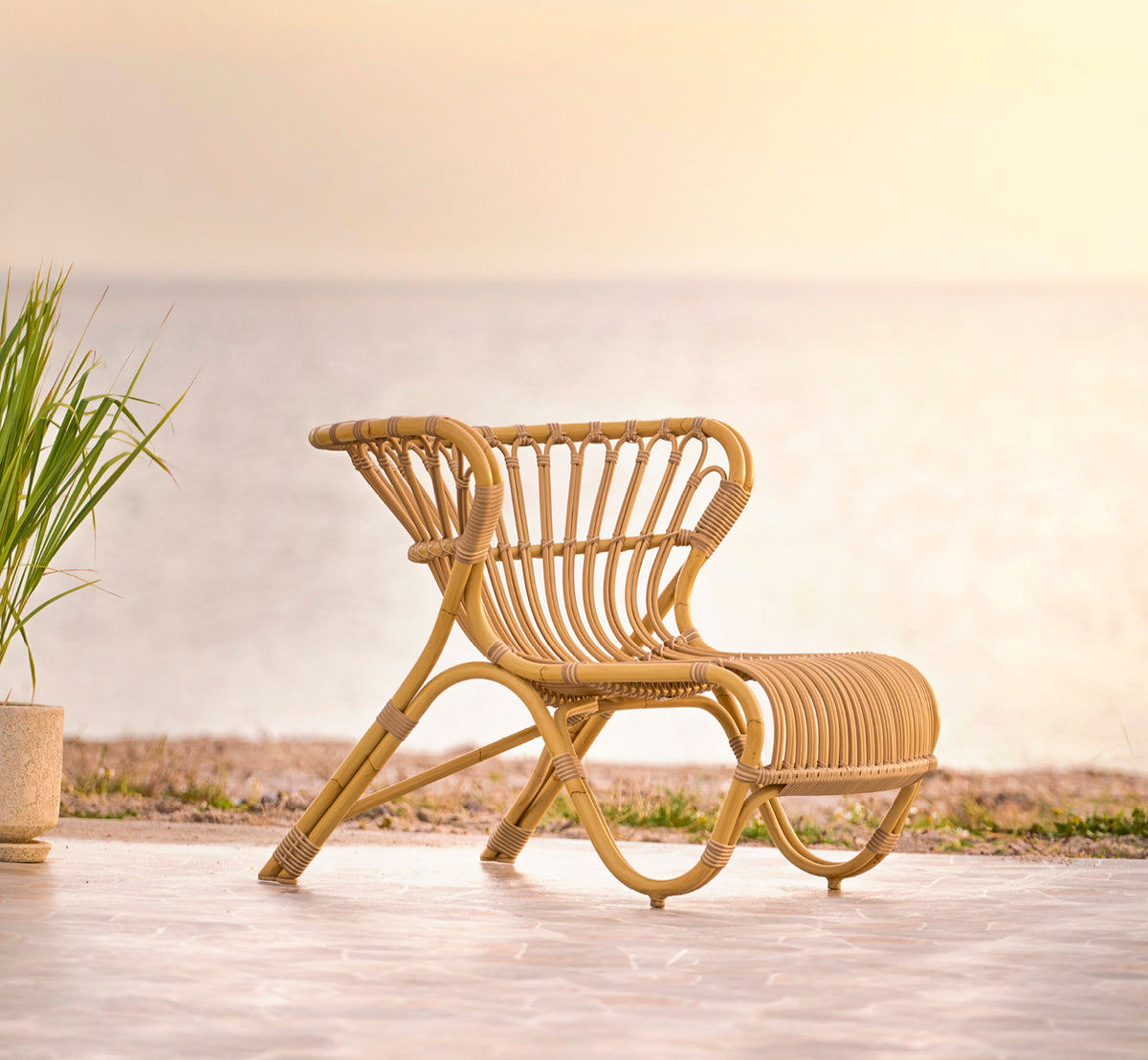 Dies ist ein Lifestyle-Bild von Fox Außen-Lounge-Sessel in natural Aluminium ArtFibre, auf einem Holzdeck am Wasser mit Küstenschilf und Meerblick.