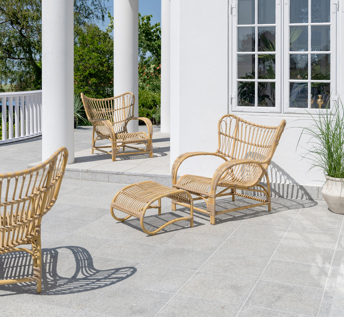 Dies ist ein Lifestyle-Bild von Teddy Außen-Lounge-Sessel in natural aluminium artfibre. Auf einer sonnigen gepflasterten Terrasse an einem weiß gerahmten Türrahmen platziert.
