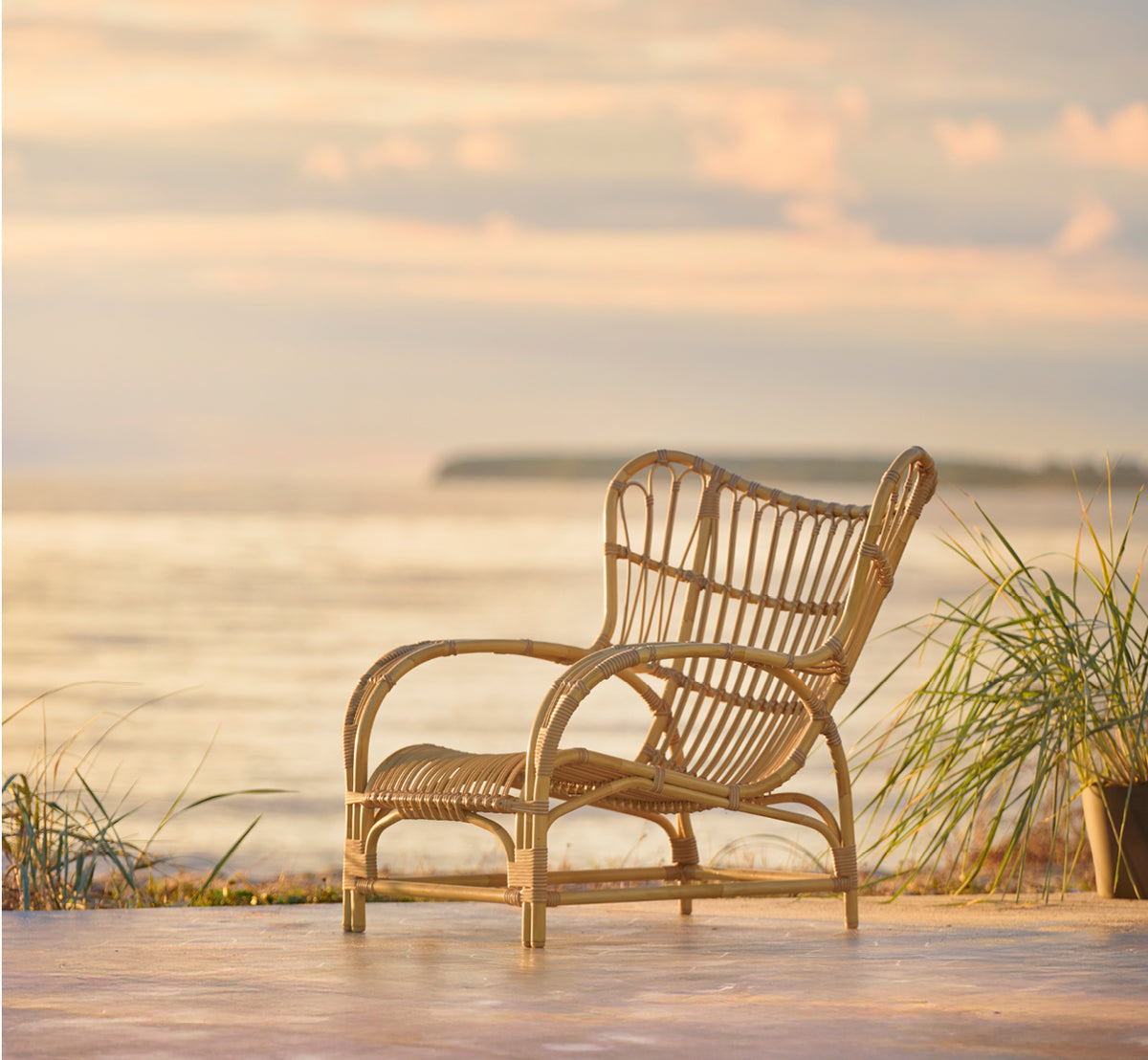 Dies ist ein Lifestyle-Bild von Teddy Außen-Lounge-Sessel in natural aluminium artfibre. Auf einer sonnigen gepflasterten Terrasse an einem weiß gerahmten Türrahmen platziert.