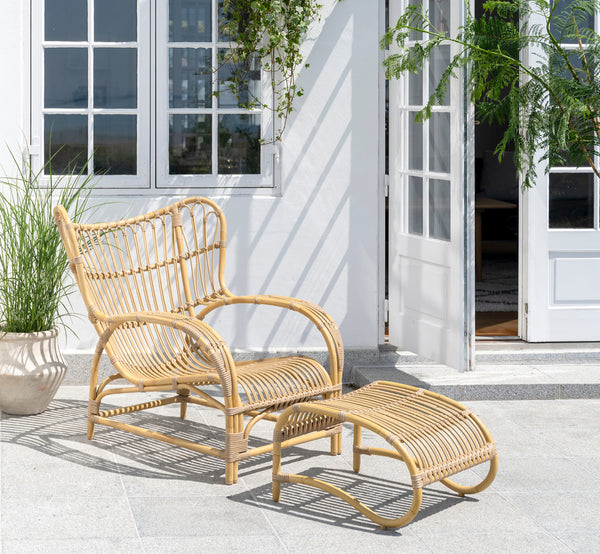 Dies ist ein Lifestyle-Bild von Teddy Außen-Fußhocker in natural aluminium artfibre. Mit dem passenden Loungesessel auf einer sonnigen gepflasterten Terrasse kombiniert.