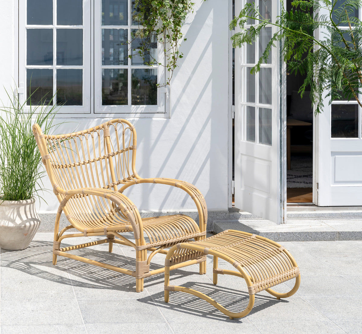 Dies ist ein Lifestyle-Bild von Teddy Außen-Fußhocker in natural aluminium artfibre. Mit dem passenden Loungesessel auf einer sonnigen gepflasterten Terrasse kombiniert.
