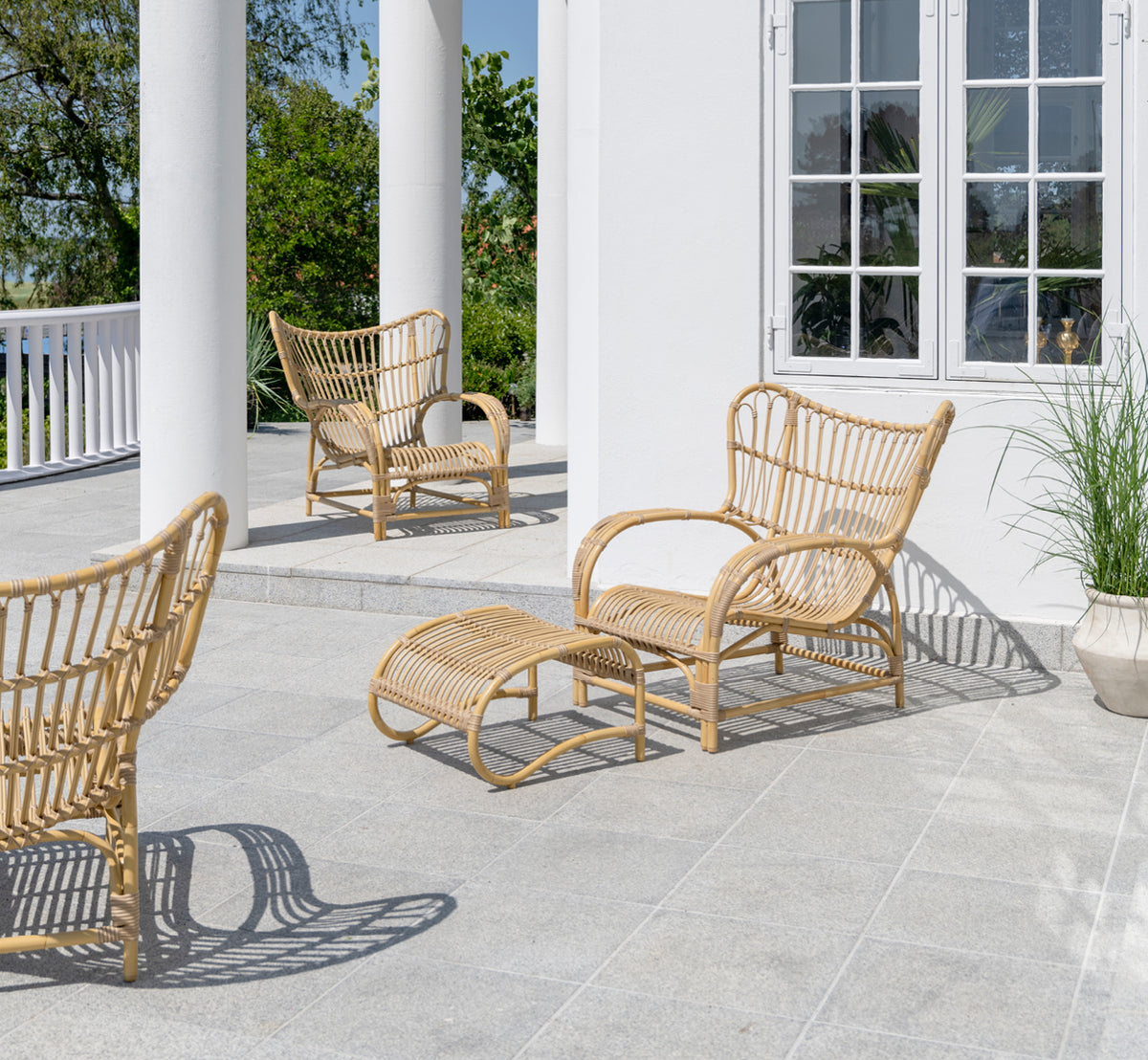 Dies ist ein Lifestyle-Bild von Teddy Außen-Fußhocker in natural aluminium artfibre. Mit dem passenden Loungesessel auf einer sonnigen gepflasterten Terrasse kombiniert.