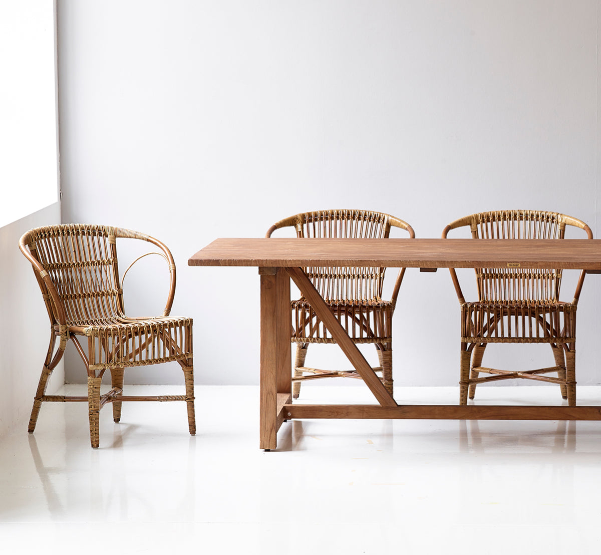 Dies ist ein Lifestyle-Bild von Robert Esszimmerstuhl in polished antique rattan. Neben einer hohen Terrakotta-Urne auf einem Fischgrätparkettboden platziert.