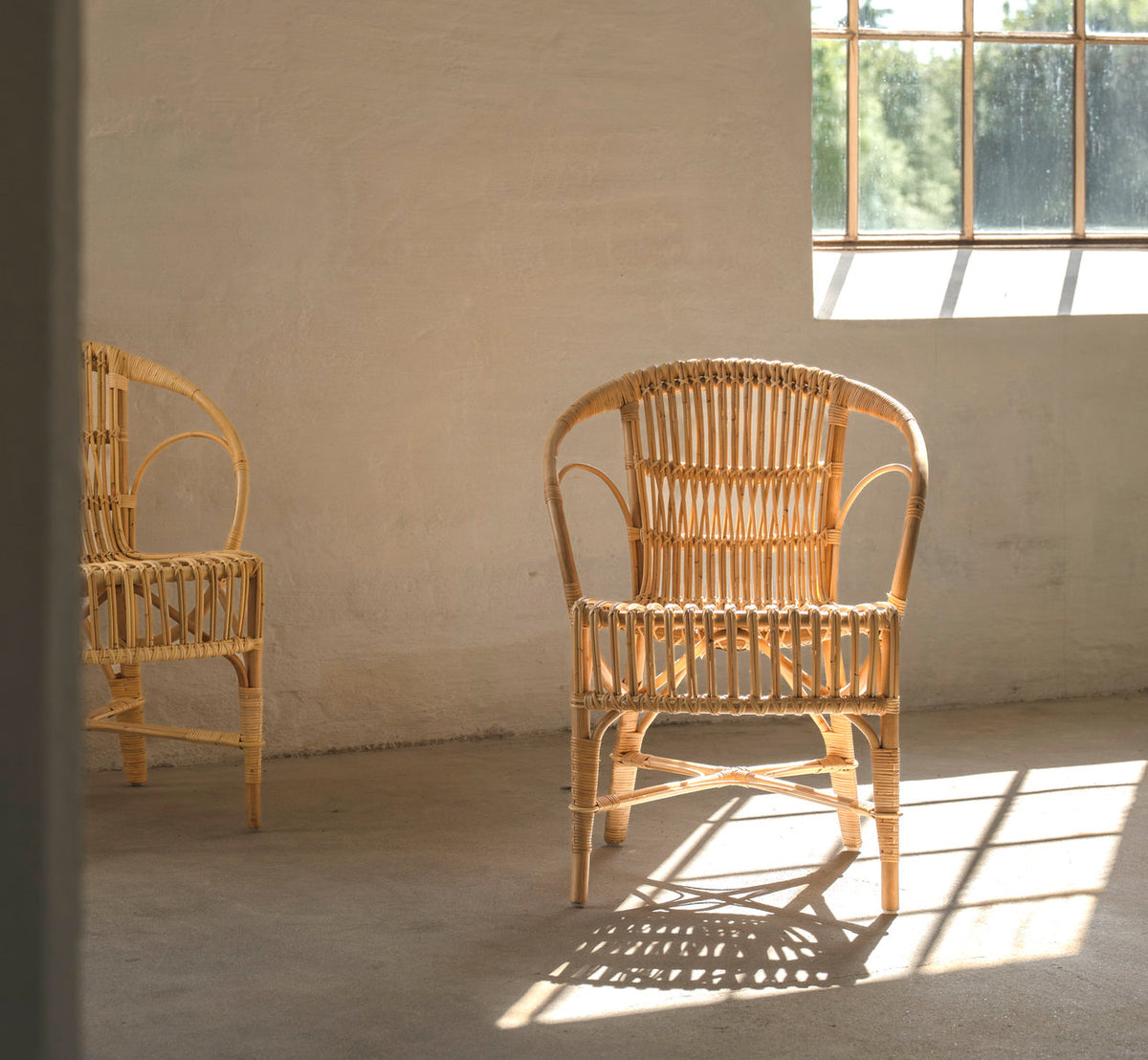 Dies ist ein Lifestyle-Bild von Robert Esszimmerstuhl in polished natural rattan. Paar in einem sonnigen Raum mit Betonboden.