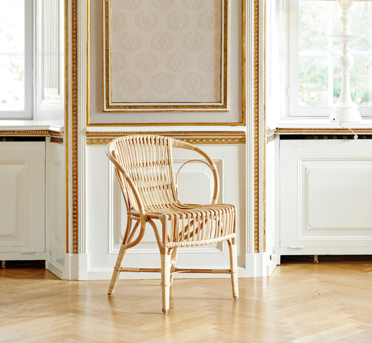 Dies ist ein Lifestyle-Bild von Robert Esszimmerstuhl in polished natural rattan. Neben einem Säulentisch mit Tulpen auf einem Juteteppich platziert.