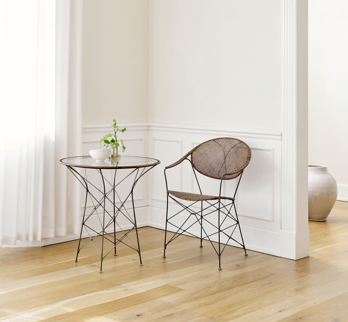 Dies ist ein Lifestyle-Bild von Funky Esszimmerstuhl in hazelnut rattan iron frame, in einem hellen Interieur mit weißen Wandpaneelen und.