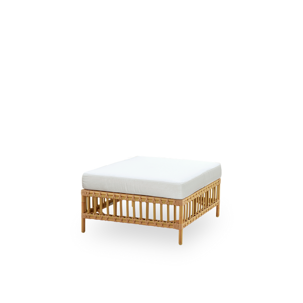 Seitenansicht des Maggie Outdoor-Sofas Pouf-Moduls in Natural-Farbe, präsentiert mit Glasplatte zur Nutzung als Beistelltisch. Aluminiumrahmen im handbemalten Rattan-Look mit ArtFibre-Umschlingungen.
